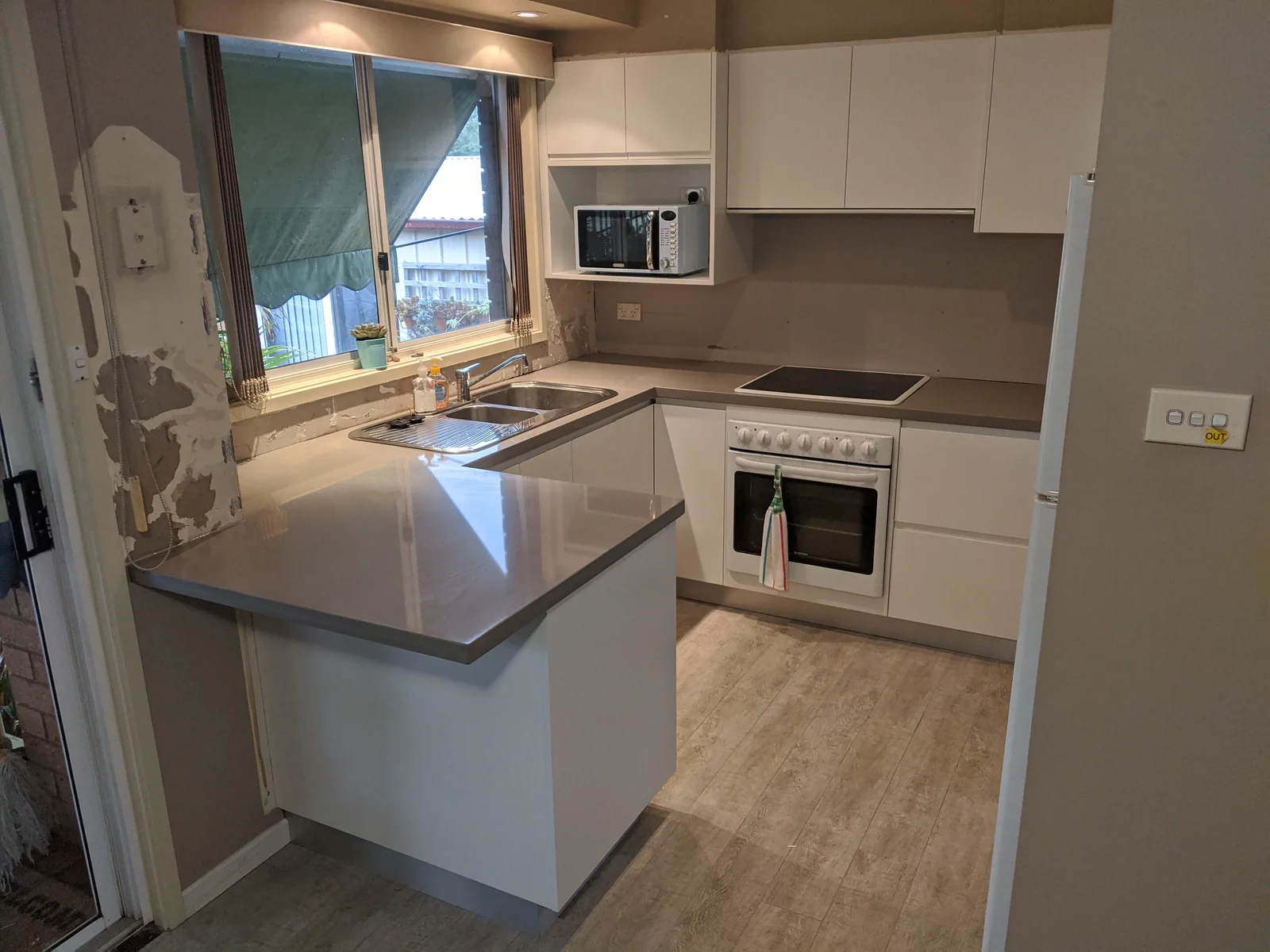Kitchen after new white cabinetry and light work surfaces were fitted, with wall finishing still in progress