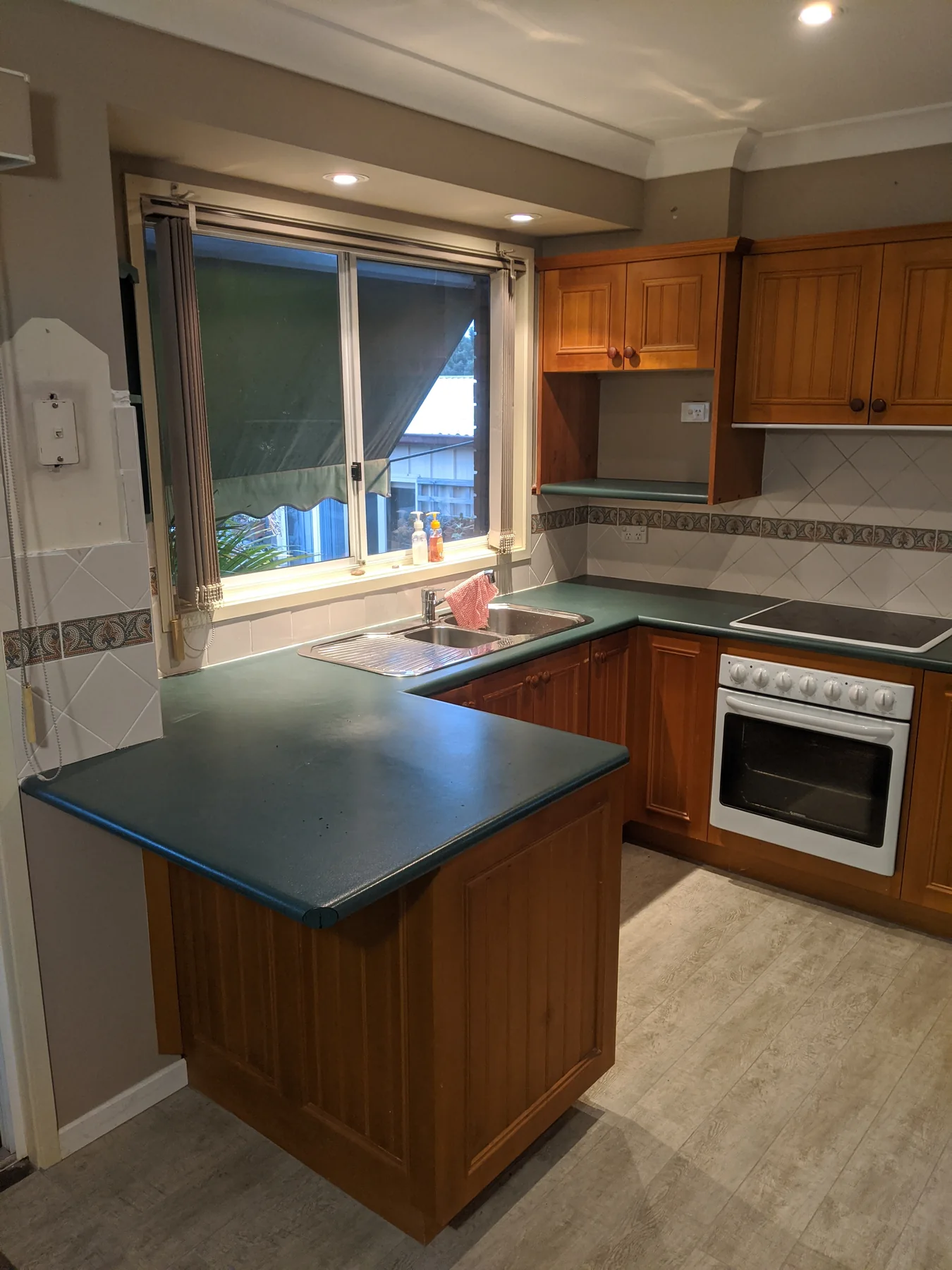 Kitchen before refurbishment, with timber doors and dark green worktops