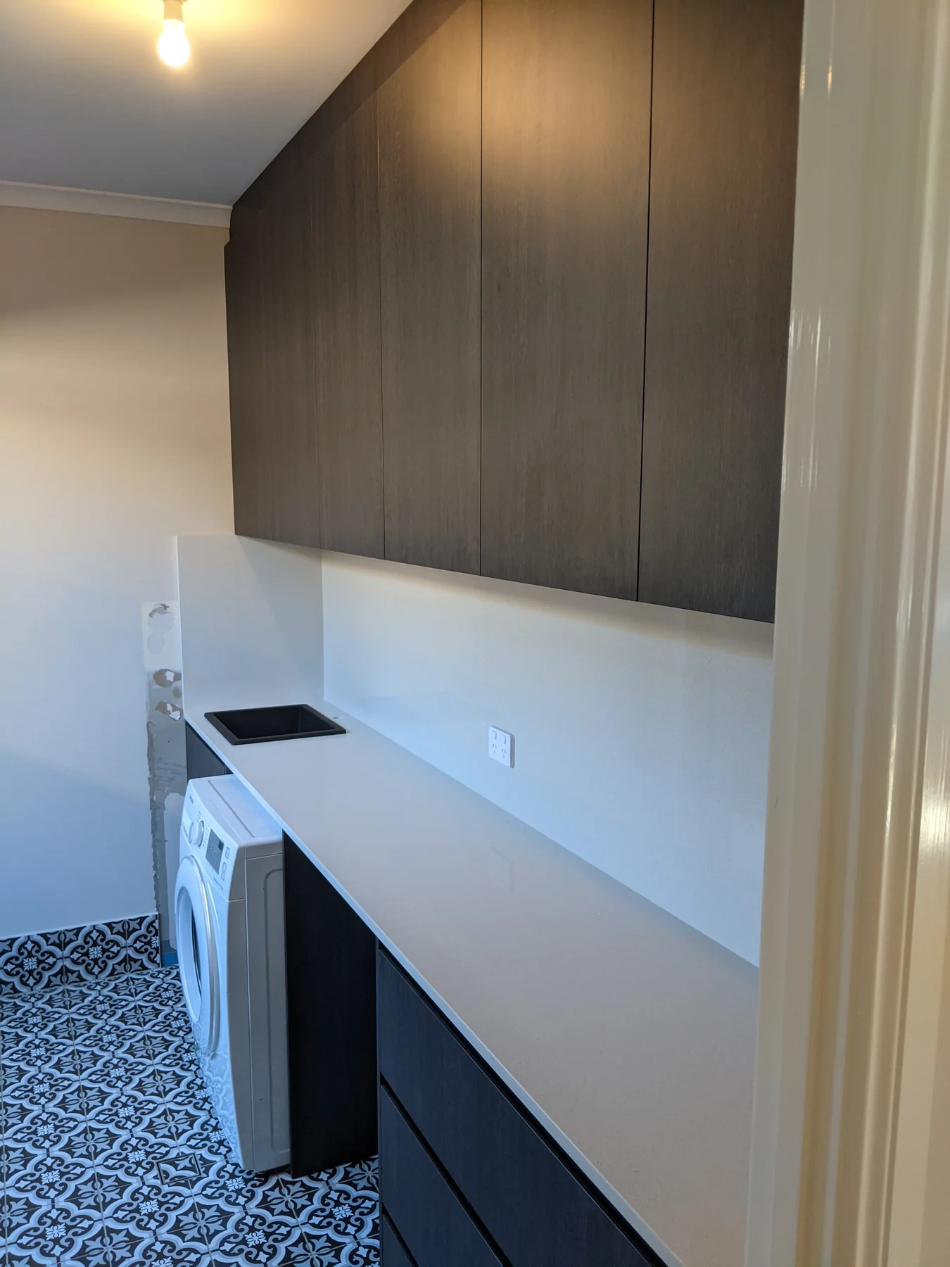 Laundry after the dark cabinetry, white work surface and black sink were fitted