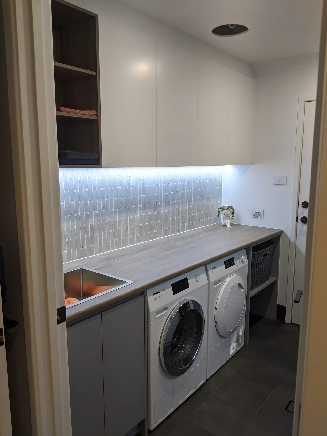 Completed laundry with dark lower cabinetry, white overhead cupboards and side-by-side appliances